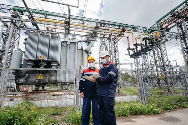 Engineers electrical substations conduct a survey of modern high-voltage equipment in the mask at the time of pandemia. Energy. Industry