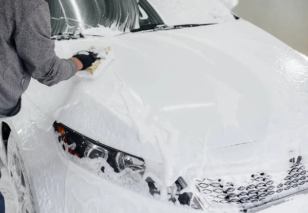 Modern washing with foam and high-pressure water of a white car. Car wash