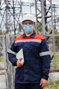 Bir elektrik santrali mühendisi Pondemia zamanında maske takan modern yüksek voltajlı ekipmanları inceliyor. Enerji. Sanayi