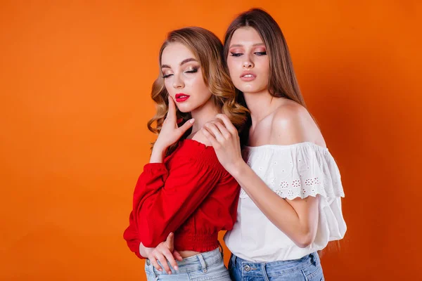 两个年轻貌美的女孩带着橙色的背景在演播室里表现出感情和微笑 女孩做广告 — 图库照片