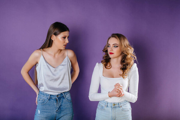 Two young and beautiful girls shows emotions and smiles in the Studio on a purple background. Girls for advertising