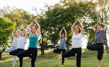 Bir grup insan gün batımında parkta yoga yapıyor. Sağlıklı yaşam tarzı, meditasyon ve sağlık