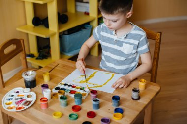 Odasında küçük sevimli bir çocuk oynuyor ve resim yapıyor. Eğlence ve eğlence. Evde kal.