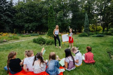 Bir öğretmen açık hava parkında bir sınıf çocuğa ders veriyor. Okula dönüyorum, salgın sırasında öğreniyorum.