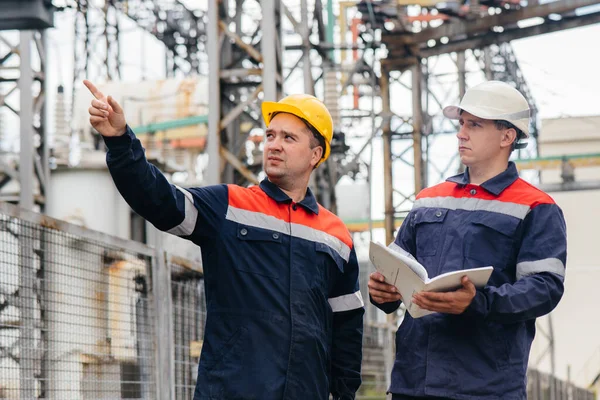 İki uzman elektrik santrali mühendisi modern yüksek voltajlı ekipmanları inceliyor. Enerji. Sanayi