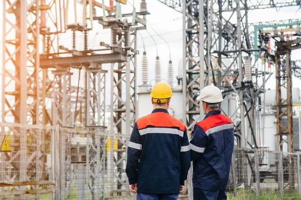 İki uzman elektrik santrali mühendisi günbatımında modern yüksek voltajlı ekipmanları inceliyor. Enerji. Sanayi