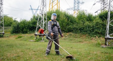 Elektirik santralinin bölgesinde çim biçen genç bir adam. Girişimdeki çim temizleme, yangın güvenlik önlemlerinin uygulanması