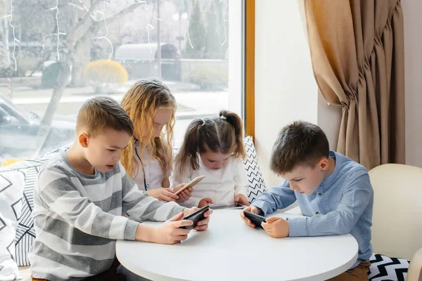 Çocuklar bir kafede bir masada oturup birlikte cep telefonu oynarlar. Modern eğlence
