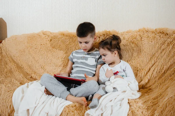 Brother and sister play on the couch in the tablet