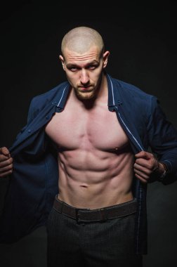 Tarz sahibi, kel genç bir adam çıplak bir gövdeyle kategoride karanlık bir arkaplanda duruyor.