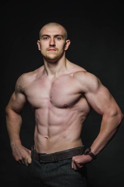 Sportif seksi adam karanlık bir zeminde üstsüz duruyor. Spor, güzellik