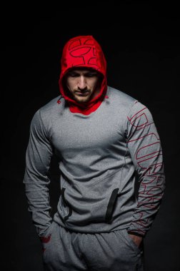 Stüdyoda kapüşonlu karanlık bir arka plana karşı duran sportif bir adam. Spor, güzellik