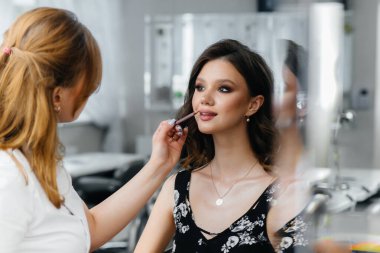 Güzel, modern bir güzellik salonunda, profesyonel bir makyöz genç bir kız için makyaj yapar. Güzellik ve moda.