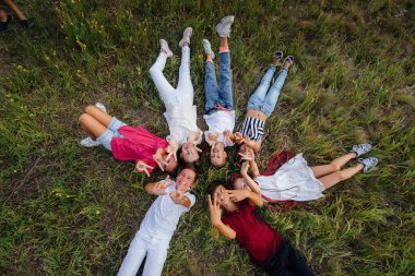 Bir grup mutlu çocuk çimde bir çember şeklinde uzanıyor ve mutlu bir şekilde gülümsüyor. Mutlu çocukluk