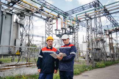 İki uzman elektrik santrali mühendisi modern yüksek voltajlı ekipmanları inceliyor. Enerji. Sanayi