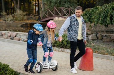 Bir baba gün batımında küçük çocuklarına Segway 'e binmeyi öğretir. Park 'ta aile tatili.