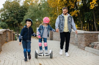 Bir baba gün batımında küçük çocuklarına Segway 'e binmeyi öğretir. Park 'ta aile tatili.