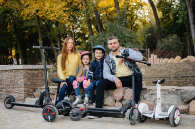 Büyük mutlu bir aile, gün batımında sıcak bir sonbahar gününde Segways ve elektrikli scooter kullanır. Park 'ta aile tatili.