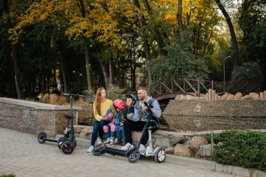 Büyük mutlu bir aile, gün batımında sıcak bir sonbahar gününde Segways ve elektrikli scooter kullanır. Park 'ta aile tatili.