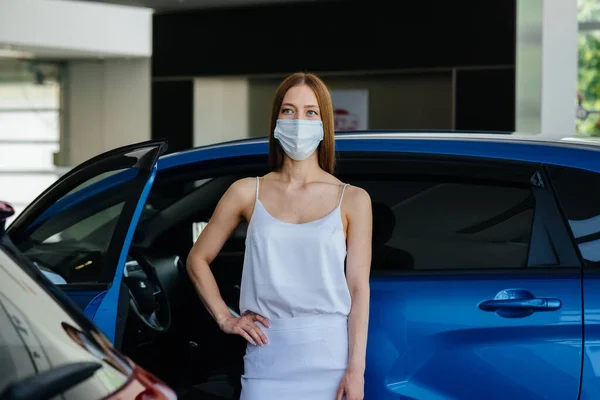 在流行病流行期间 一位年轻漂亮的姑娘戴着面具在一家汽车经销店检查一辆新车 在潘德米亚时期 汽车的销售和购买 — 图库照片