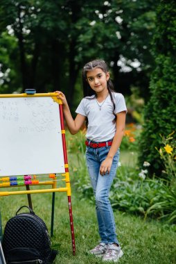 Okullu bir kız tahtaya ders yazıyor ve açık hava eğitimiyle meşgul. Okula dönüyorum, salgın sırasında öğreniyorum.