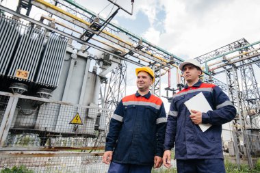 İki uzman elektrik santrali mühendisi modern yüksek voltajlı ekipmanları inceliyor. Enerji. Sanayi