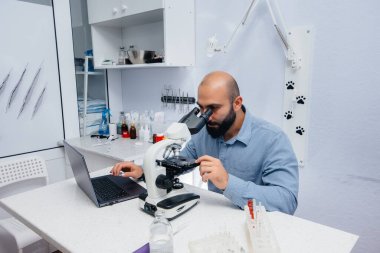 Laboratuvardaki bir erkek doktor mikroskop altında virüs ve bakterileri inceliyor. Tehlikeli virüs ve bakteri araştırmaları