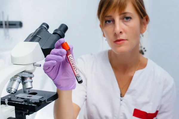 A female doctor in the laboratory holds a medical test tube with a positive test for COVID-19. Research of dangerous viruses and bacteria