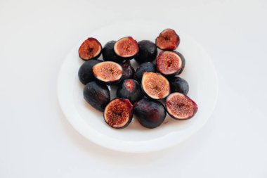 Olgun ve tatlı incirler kesilip beyaz arka planda bir tabağa yerleştirilmiş ve boş alan bırakılmış. Meyve ve vejetaryenlik