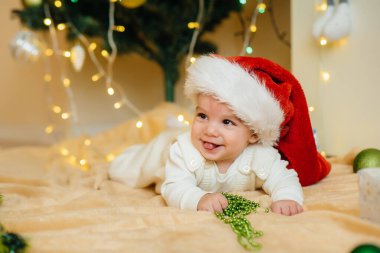 Sevimli gülümseyen bebek, Noel ağacının altında yatıyor ve hediyelerle oynuyor. Noel ve Yeni Yıl kutlamaları