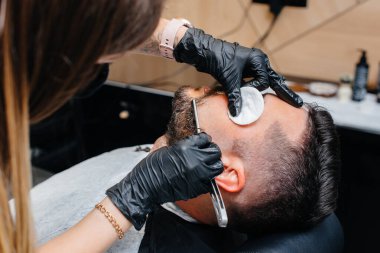 Modern bir berber dükkanında profesyonel bir stilist genç bir adamın saçını traş eder ve keser. Güzellik salonu, kuaför salonu