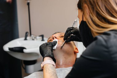 Modern bir berber dükkanında profesyonel bir stilist genç bir adamın saçını traş eder ve keser. Güzellik salonu, kuaför salonu