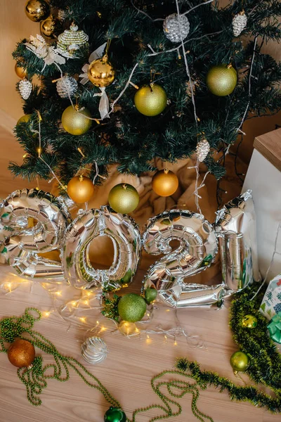 Mutlu yıllar 2021. Noel ağacıyla süslenmiş ampullerin ve çelenklerin arka planında 2021 numaralı gümüşten metal balonlar.