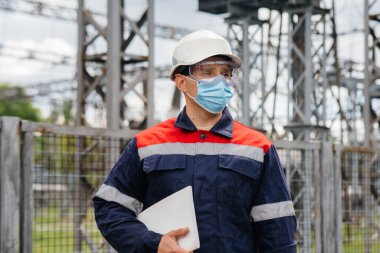 Bir elektrik santrali mühendisi Pondemia zamanında maske takan modern yüksek voltajlı ekipmanları inceliyor. Enerji. Sanayi