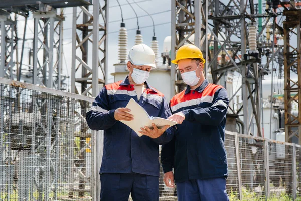 Engineers electrical substations conduct a survey of modern high-voltage equipment in the mask at the time of pandemia. Energy. Industry