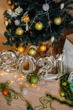 Mutlu yıllar 2021. Noel ağacıyla süslenmiş ampullerin ve çelenklerin arka planında 2021 numaralı gümüşten metal balonlar.