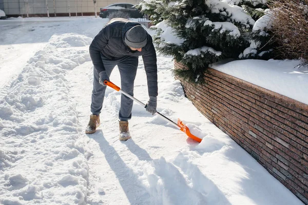 晴れた日に若い男が家の前で雪をクリアします 雪から街をきれいにする — ストック写真