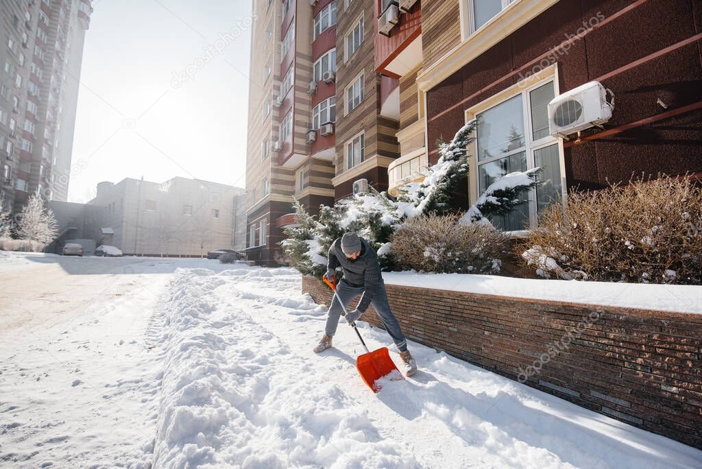 A young man clears the snow in front of the house on a sunny and frosty day. Cleaning the street from snow.