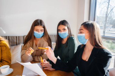 Maskeli bir grup kız bir kafede oturup dizüstü bilgisayarlarla çalışıyor. Öğrenciler.