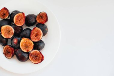 Olgun ve tatlı incirler kesilip beyaz arka planda bir tabağa yerleştirilmiş ve boş alan bırakılmış. Meyve ve vejetaryenlik