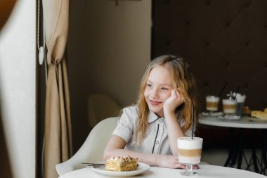 Küçük tatlı bir kız bir kafede oturuyor ve yakın plan kek ve kakaoya bakıyor. Diyet ve uygun beslenme