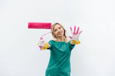 Genç bir kız beyaz bir duvar boyamadan önce pembe bir silindirle poz veriyor. İç kısmın tamiri.