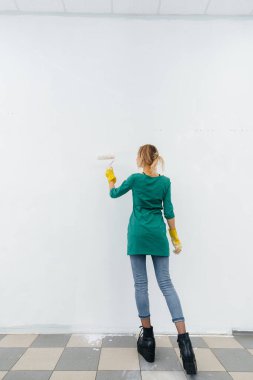 Genç bir kız silindirle beyaz bir duvar boyuyor. İç kısmın tamiri.