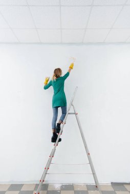 Merdivendeki genç bir kız beyaz bir duvarı silindirle boyuyor. İç kısmın tamiri.