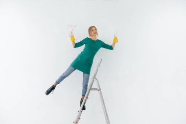 Merdivenlerdeki genç bir kız silindirle beyaz bir duvar boyuyor. İç kısmın tamiri.