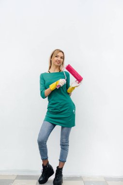 Genç bir kız beyaz bir duvar boyamadan önce pembe bir silindirle poz veriyor. İç kısmın tamiri.