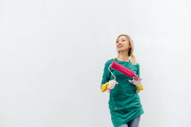 Genç bir kız beyaz bir duvar boyamadan önce pembe bir silindirle poz veriyor. İç kısmın tamiri.