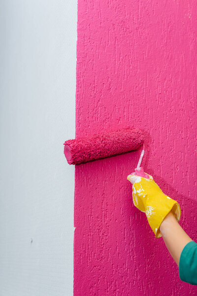 Молодая девушка красит белую стену в розовый цвет крупным планом. Ремонт интерьера.