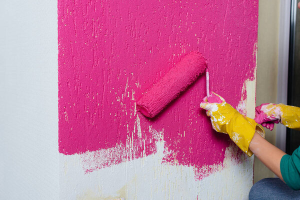Молодая девушка красит белую стену в розовый цвет крупным планом. Ремонт интерьера.
