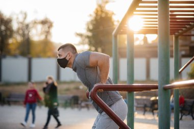 Genç bir adam gün batımında salgın sırasında spor sahasında maske takıp uyuşturucu kullanıyor. Spor, sağlıklı yaşam tarzı.